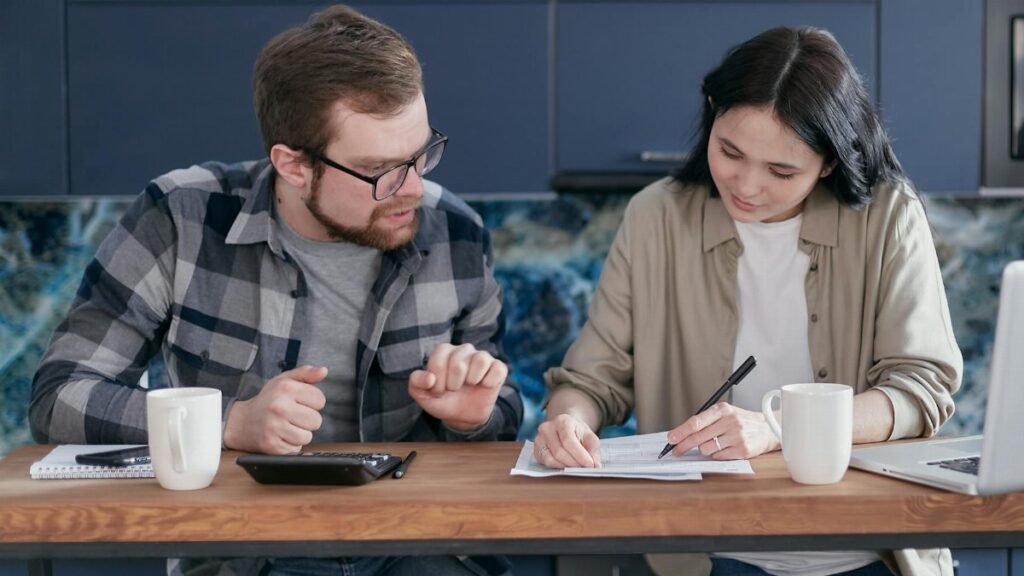 A couple sitting at a table managing their finances with a laptop and calculator, appearing focused.