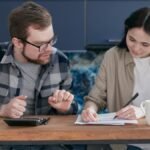A couple sitting at a table managing their finances with a laptop and calculator, appearing focused.