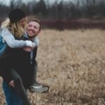 A happy couple enjoys a playful moment in a field during the day, symbolizing love and joy.