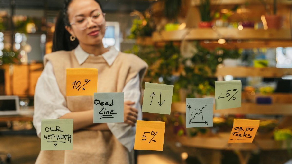 Woman analyzing sticky notes with graphs and deadlines in modern office space.