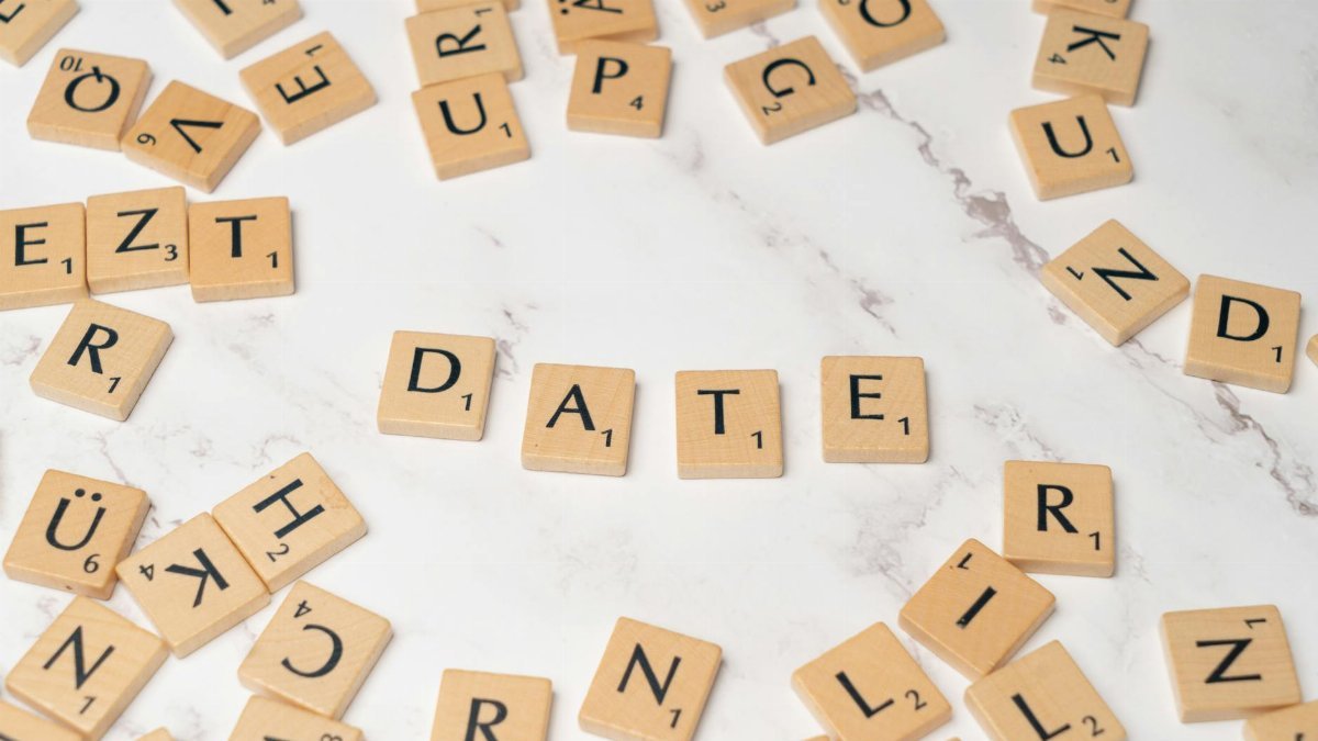 Wooden letter tiles scattered on a marble surface, spelling out 'DATE'.