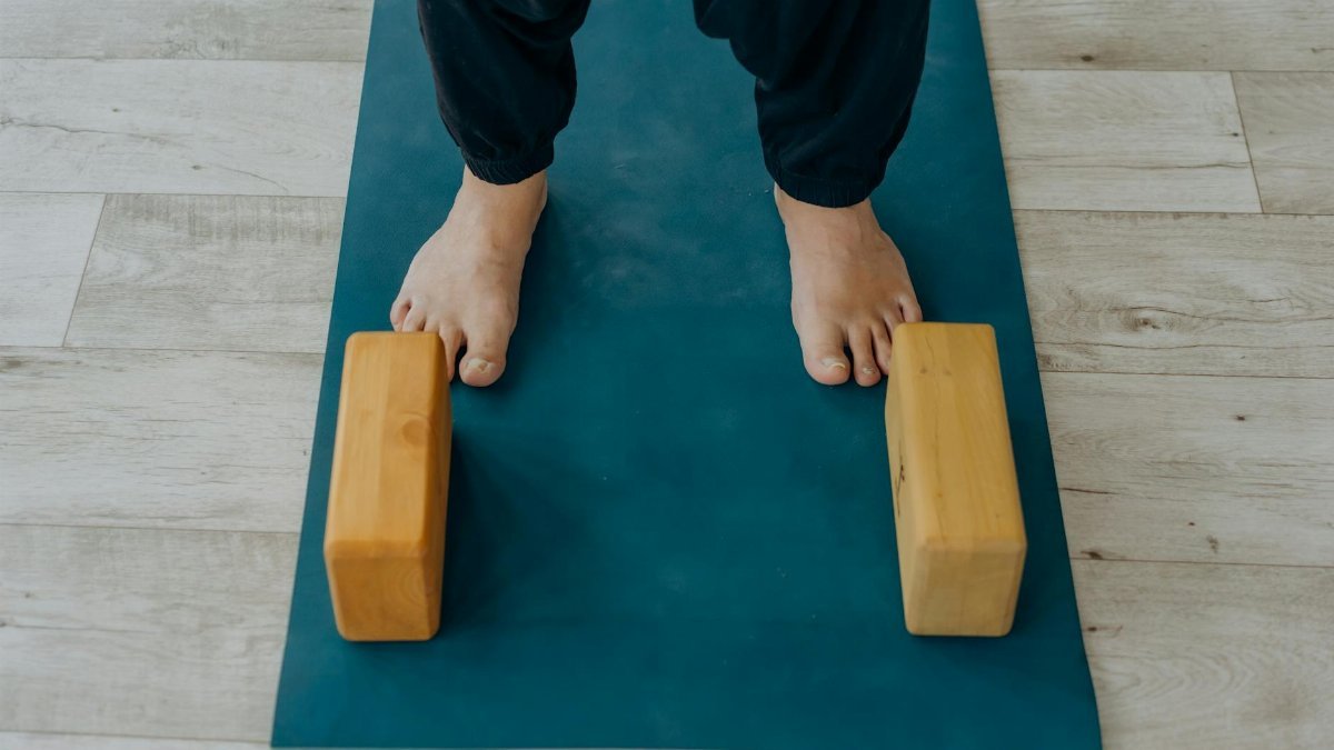 Close-up of feet on a yoga mat beside wooden blocks indoors.