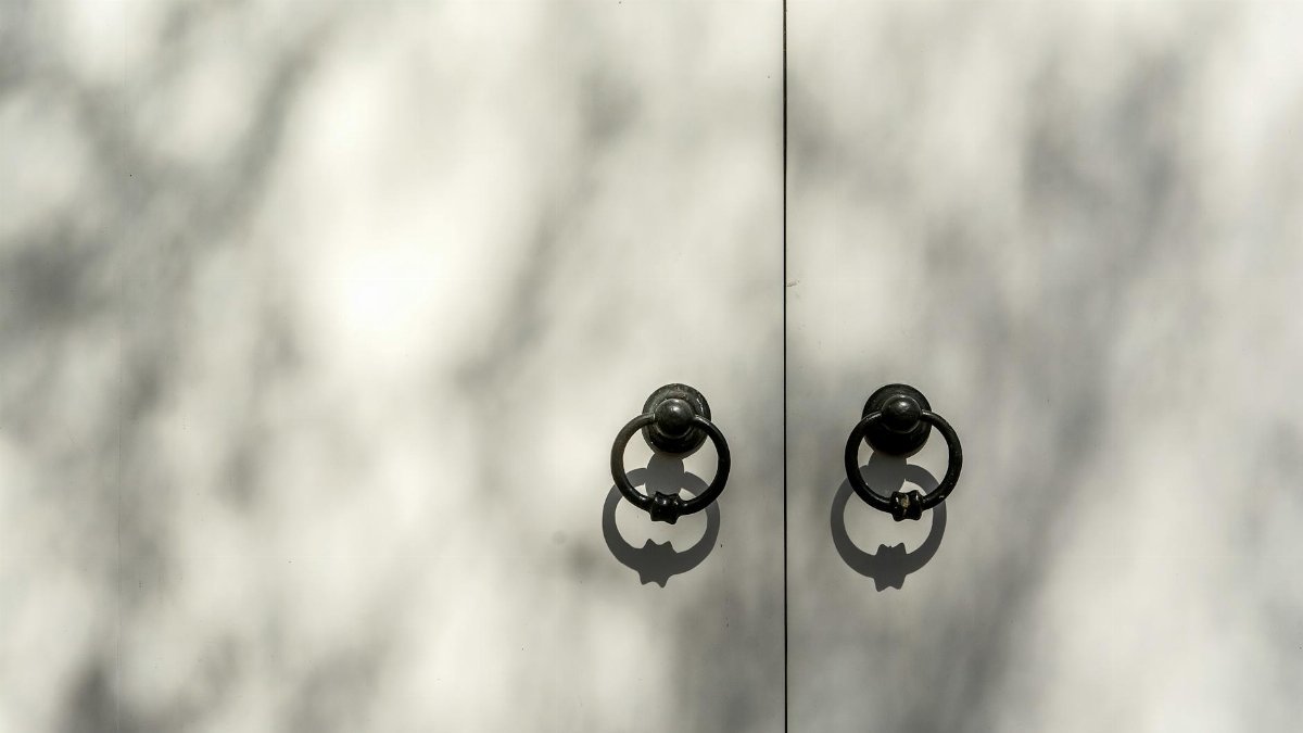 A minimalist image of dual door knockers casting shadows on a white surface, conveying an artistic feel.