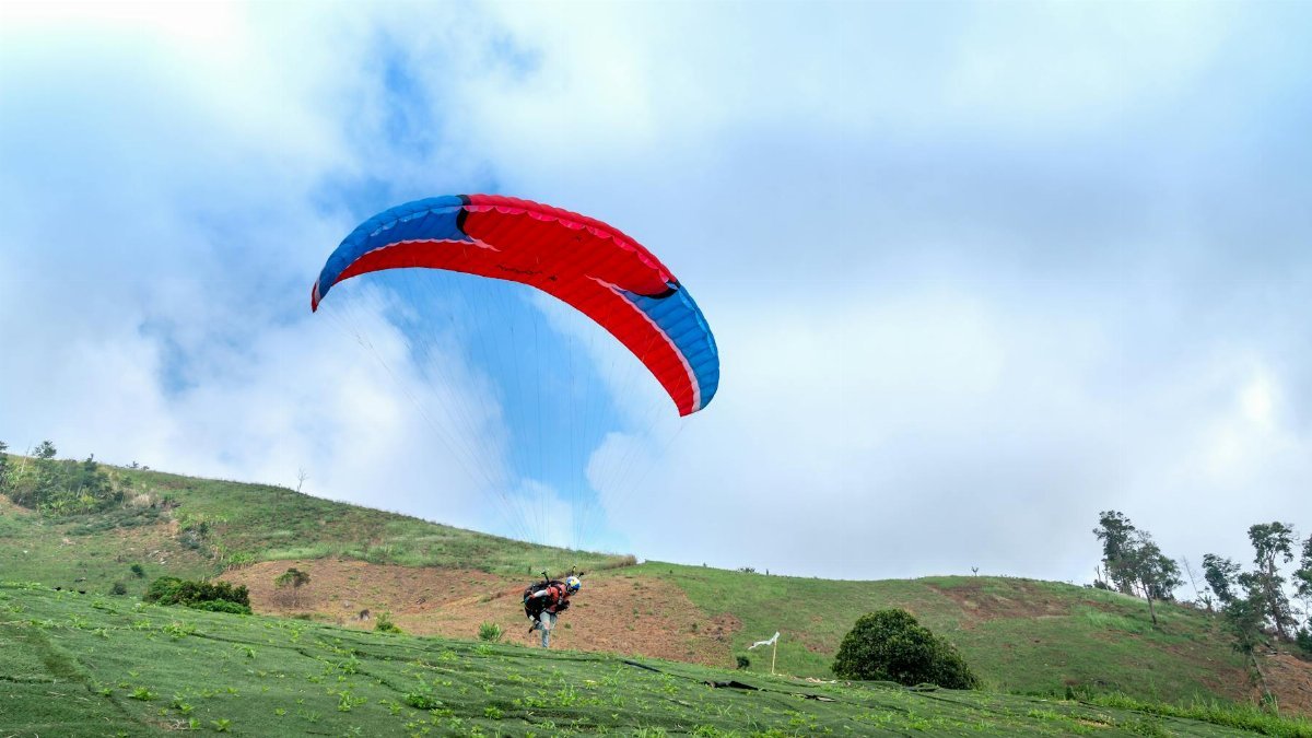 Colorful paraglider soaring over green hills, capturing the thrill of flight and freedom.