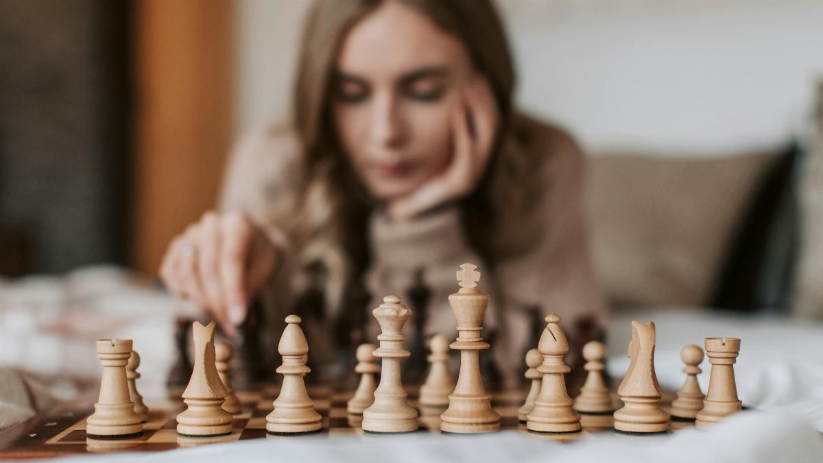 Focused woman engages in a thoughtful chess match, planning her next move on a wooden board.