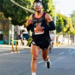 A male runner participating in an outdoor city marathon on a sunny day.