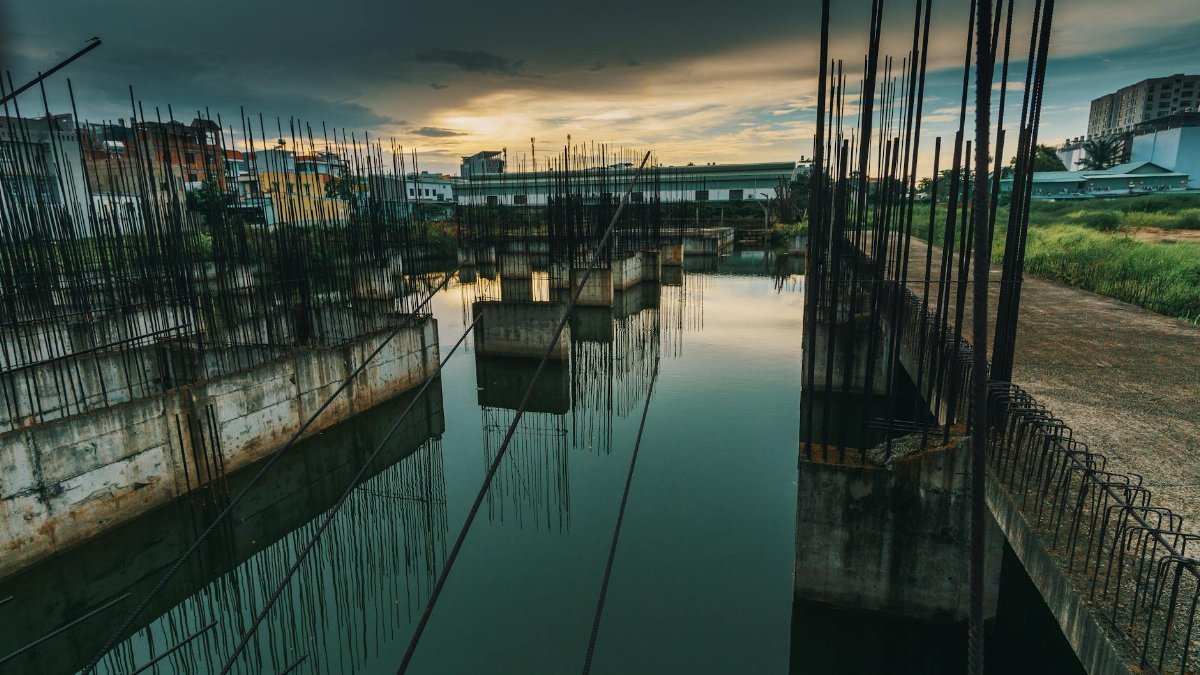 A serene view of an unfinished urban construction site reflecting on water at sunset.