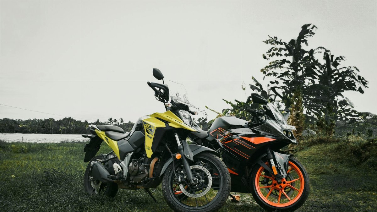 Two vibrant sport motorcycles parked on grassy field with trees and sky in background.