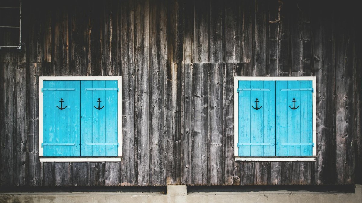 Charming wooden facade featuring two turquoise shuttered windows with anchor designs.