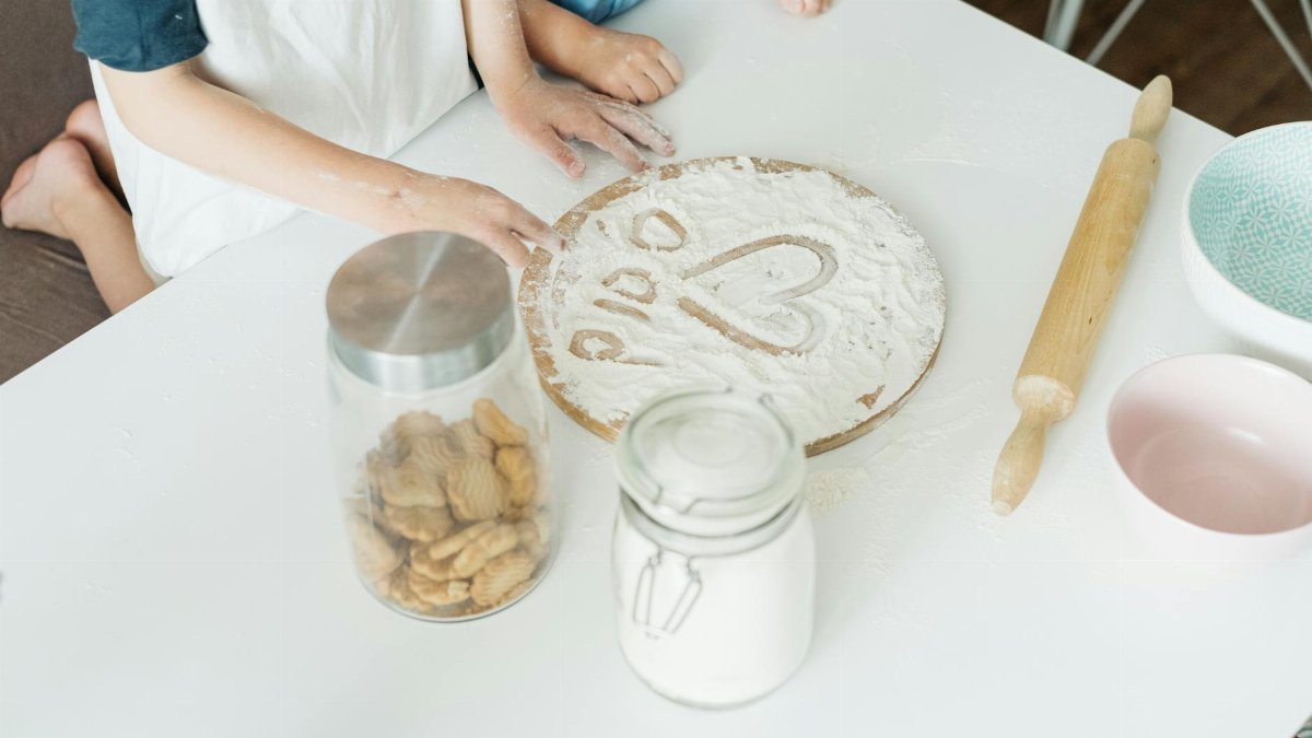 A parent and child enjoy baking together, creating a heart shape in flour as they bond.