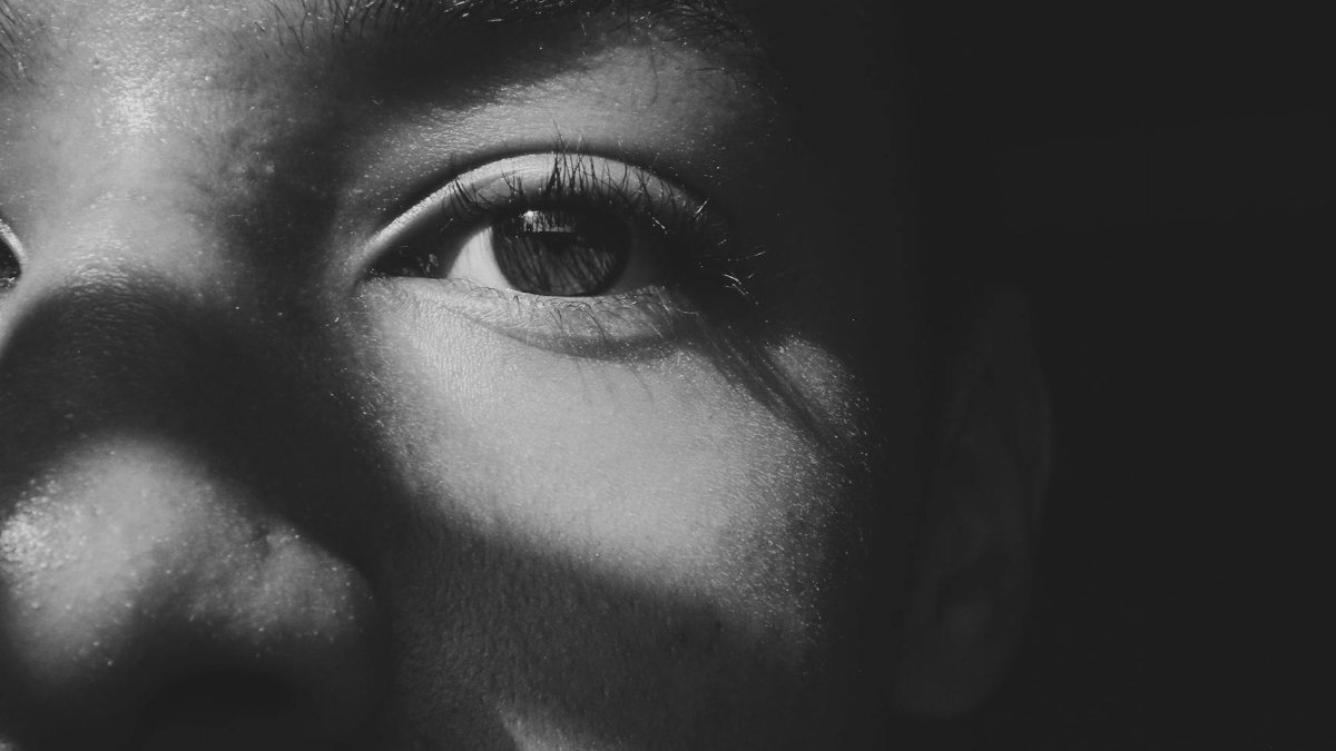 Close-up black and white photo of a person's eye with dramatic shadows casting across the face.