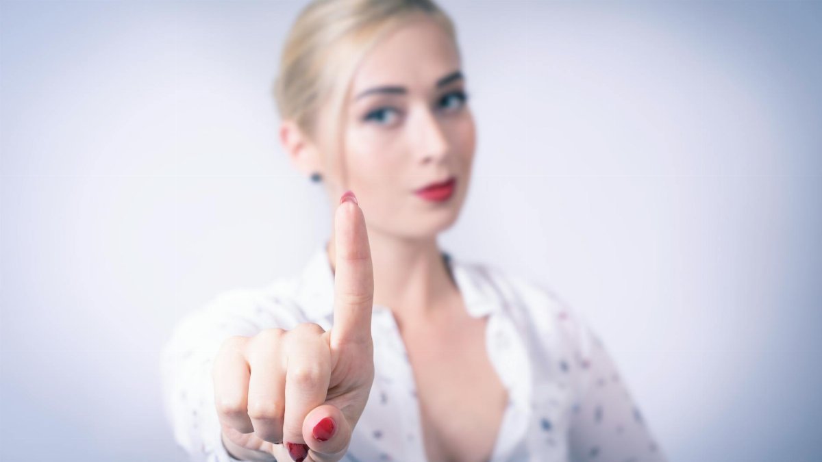Blonde woman in a studio setting pointing with focus on her red-painted finger.