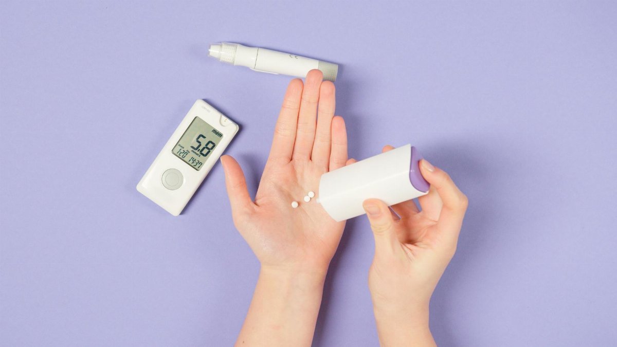 Close-up of hands using diabetes tools with a glucose monitor on a purple background.