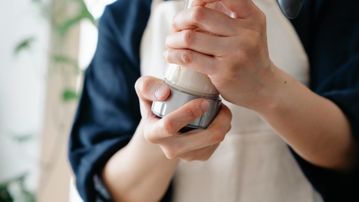 A person wearing an apron holds and shakes a protein shaker indoors. Casual food preparation scene.