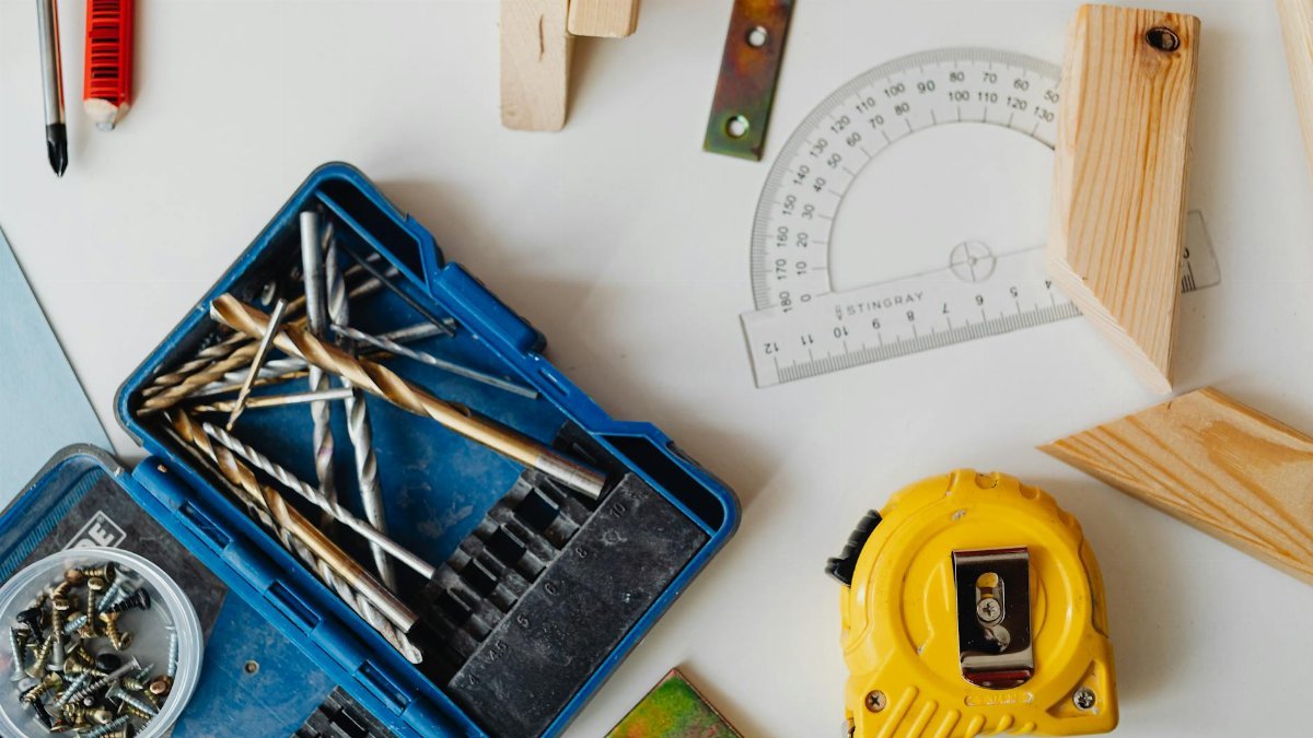 A selection of carpentry tools including drill bits, measuring tape, and protractor in an overhead shot.