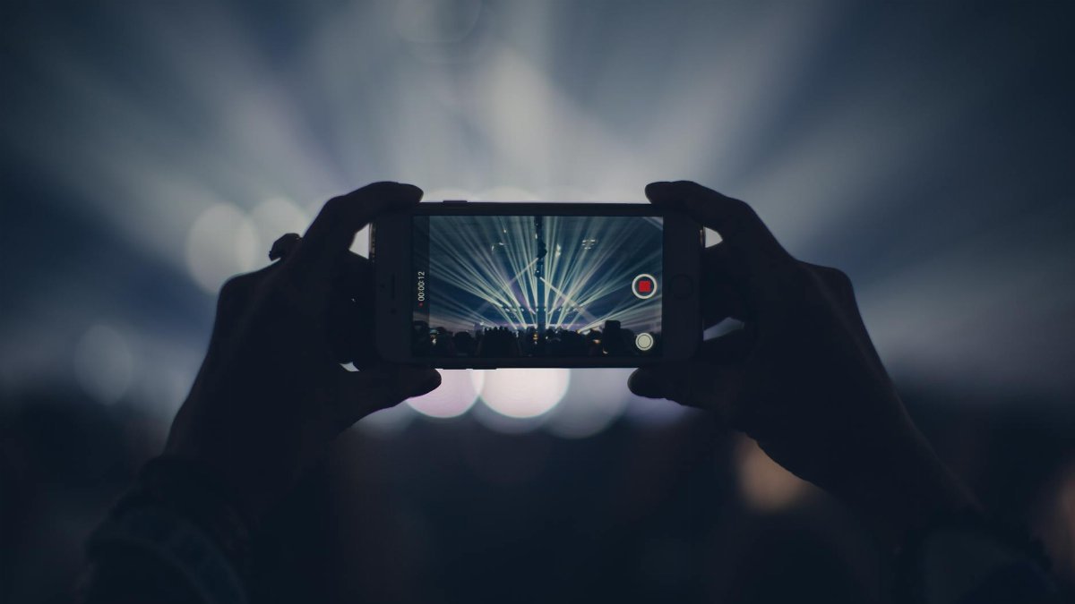 Hands holding smartphone to record concert with vibrant stage lights.