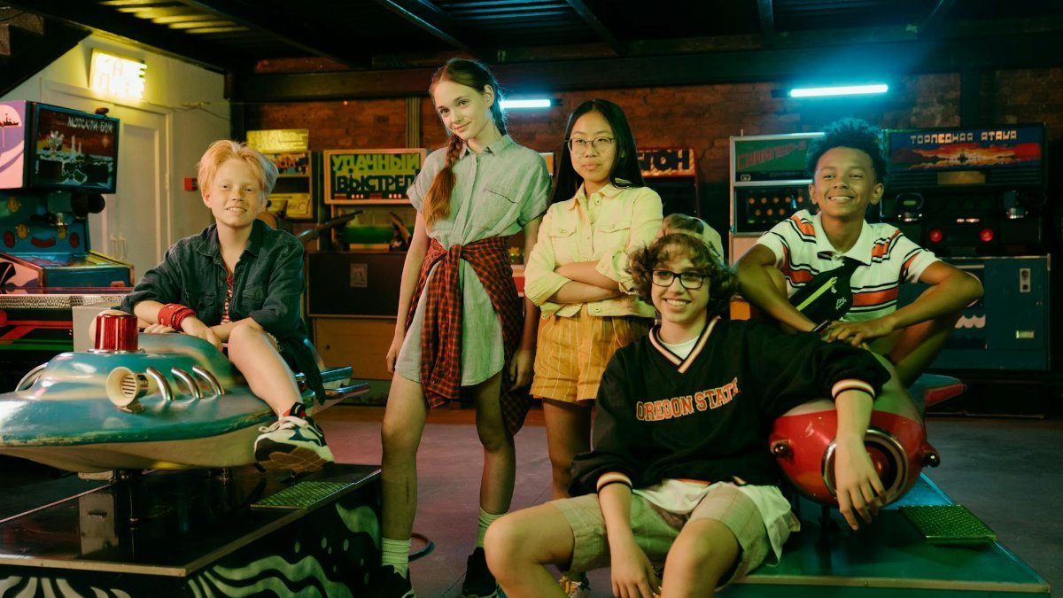 Diverse group of teens having fun in a vintage arcade with retro games and vibrant neon lights.