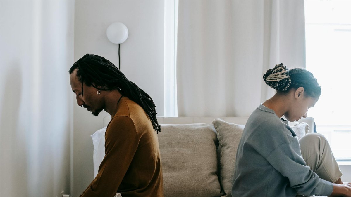Side view unhappy sorrowful African American couple sitting on bed back to back after having argument