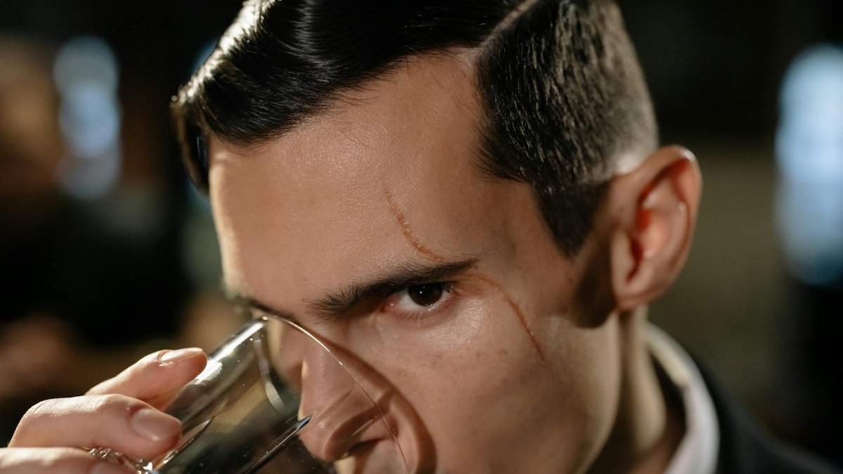 Close-up of a mysterious scarred man holding a glass, creating a noir atmosphere.