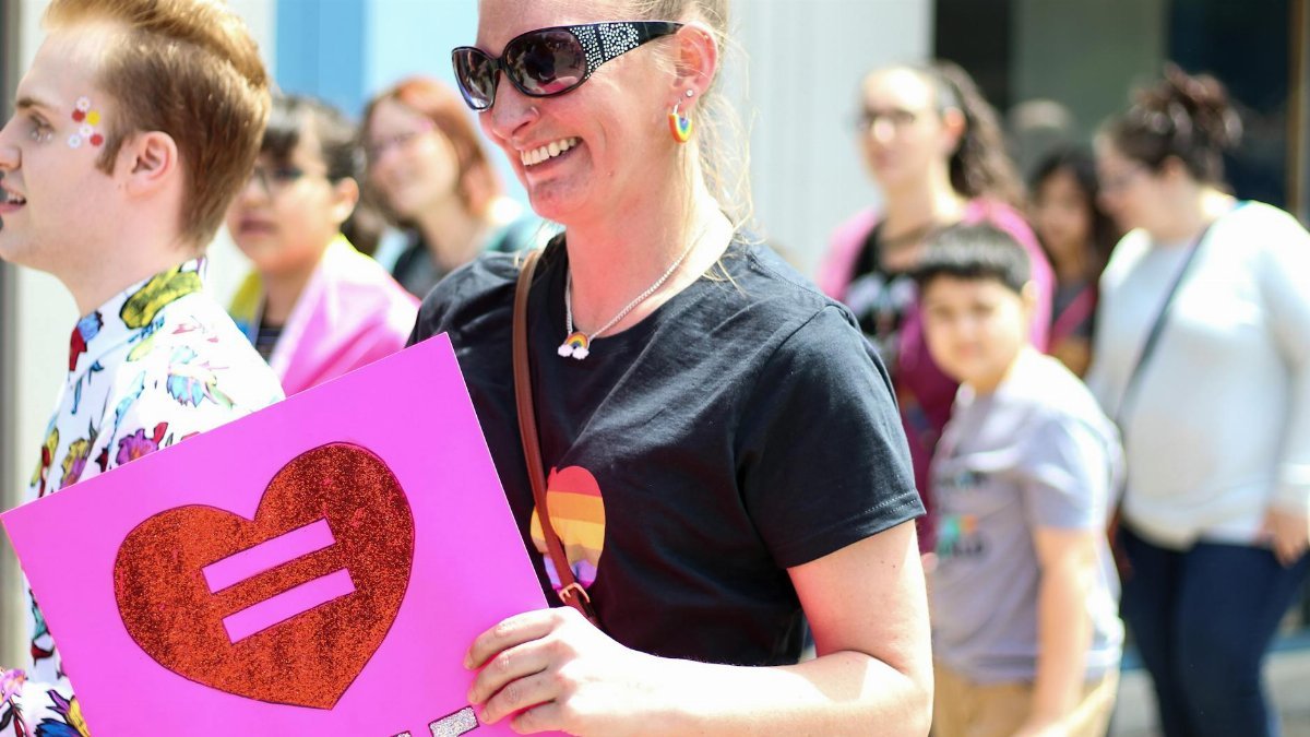 Diverse crowd celebrating LGBTQ+ equality with vibrant signs and smiles in a colorful outdoor parade.