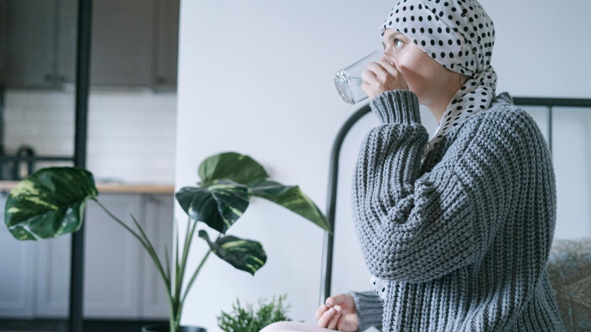 A woman wearing a headscarf drinks water indoors, promoting recovery and wellness.