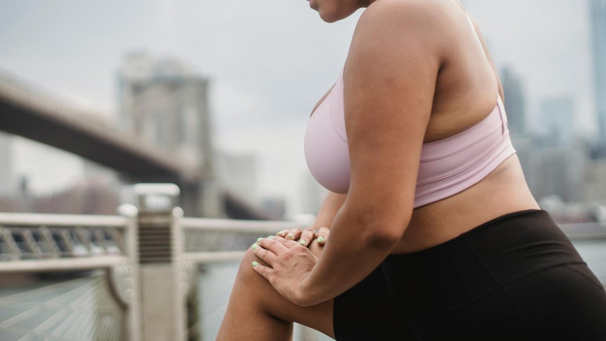 Woman in athletic wear stretching outdoors with Brooklyn Bridge in the background.