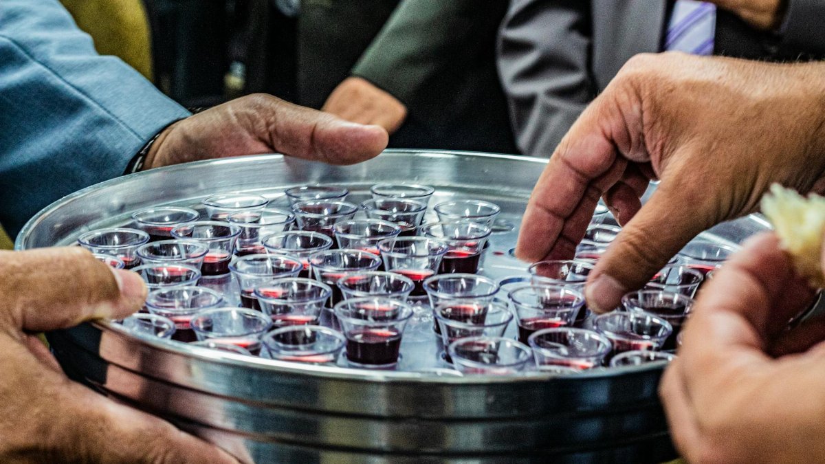 Crop anonymous male with metal tray full of small glasses of red wine for degustation