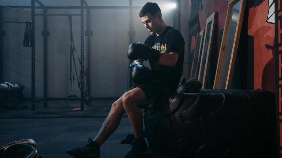 A boxer sits on a large tire in a gym, preparing for training.