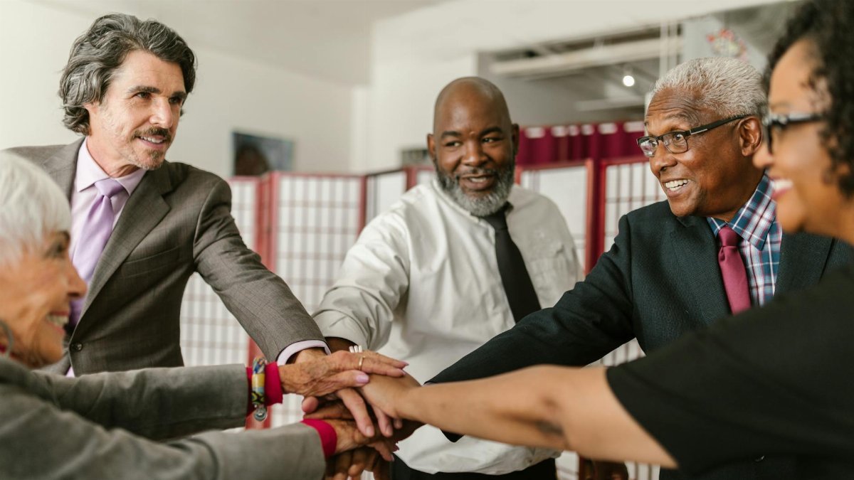 Senior business team showing unity with hands together, diverse colleagues smiling indoors.