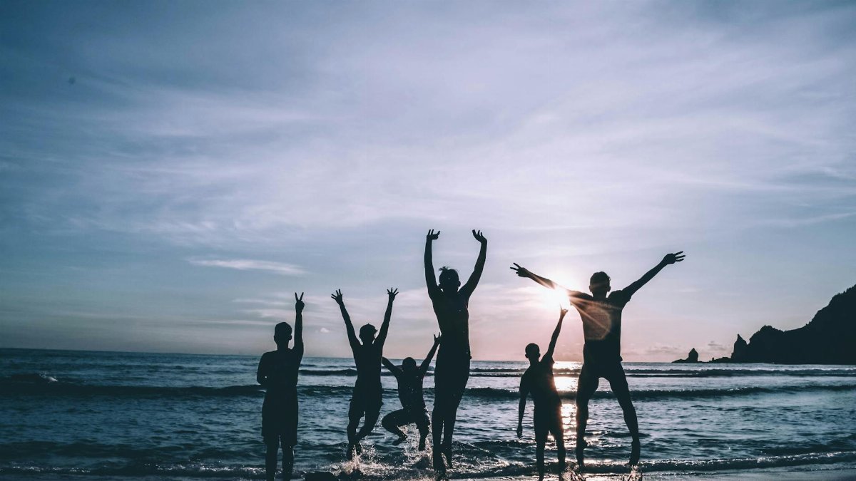 Silhouetted group of friends jumping joyfully on the beach at sunset, symbolizing freedom and happiness.