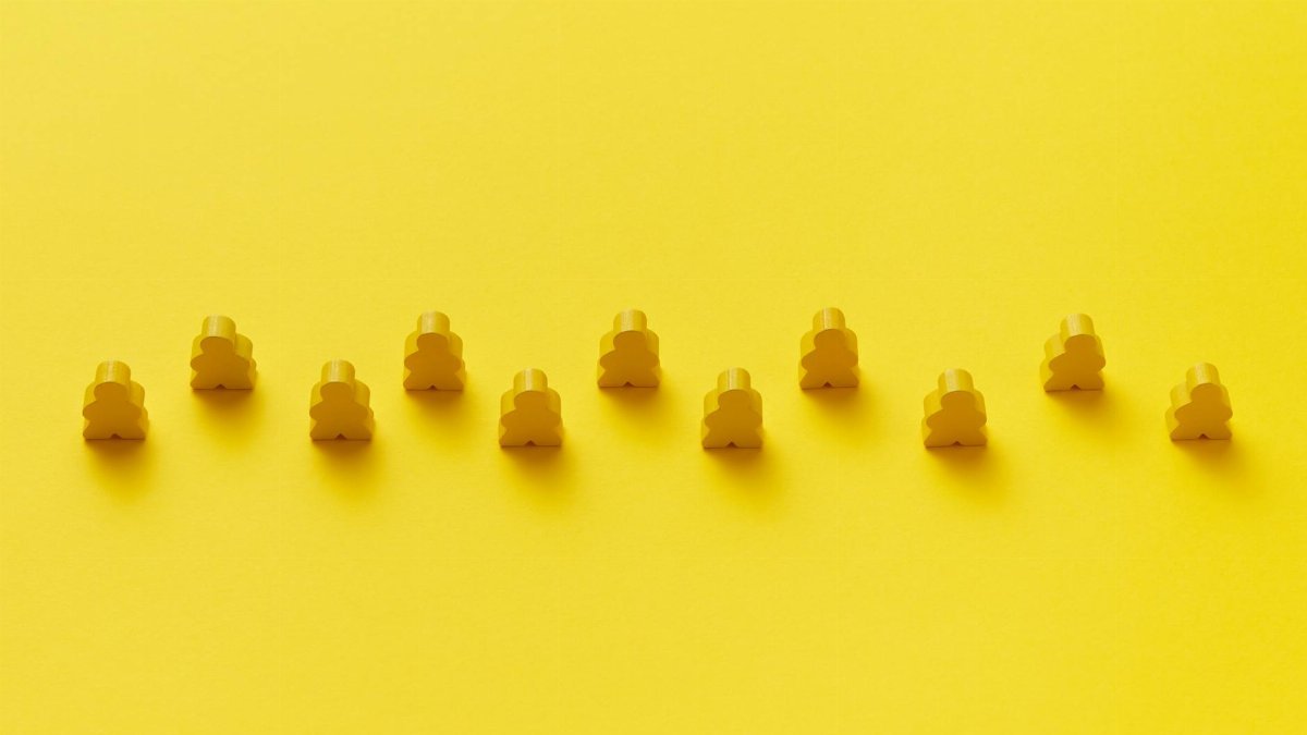 A row of yellow meeple pieces on a vibrant yellow background, showcasing uniformity and pattern.
