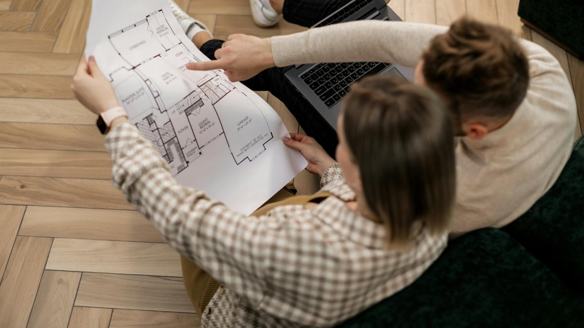 A couple examines a house blueprint together, exploring future home possibilities.