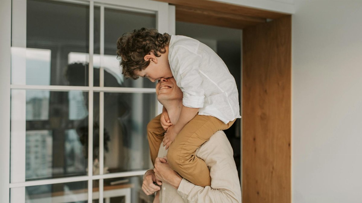 A joyful moment of a father carrying his son on his shoulders indoors, enjoying family time.