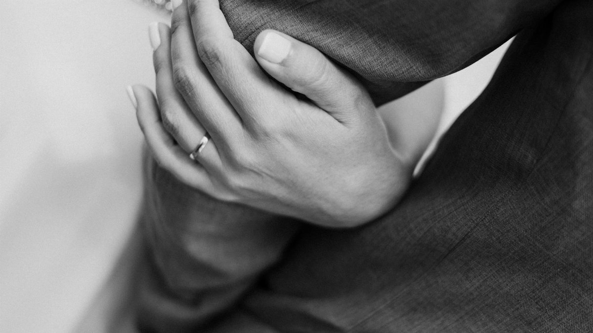 Intimate black and white close-up of a hand with a ring gently holding an arm.