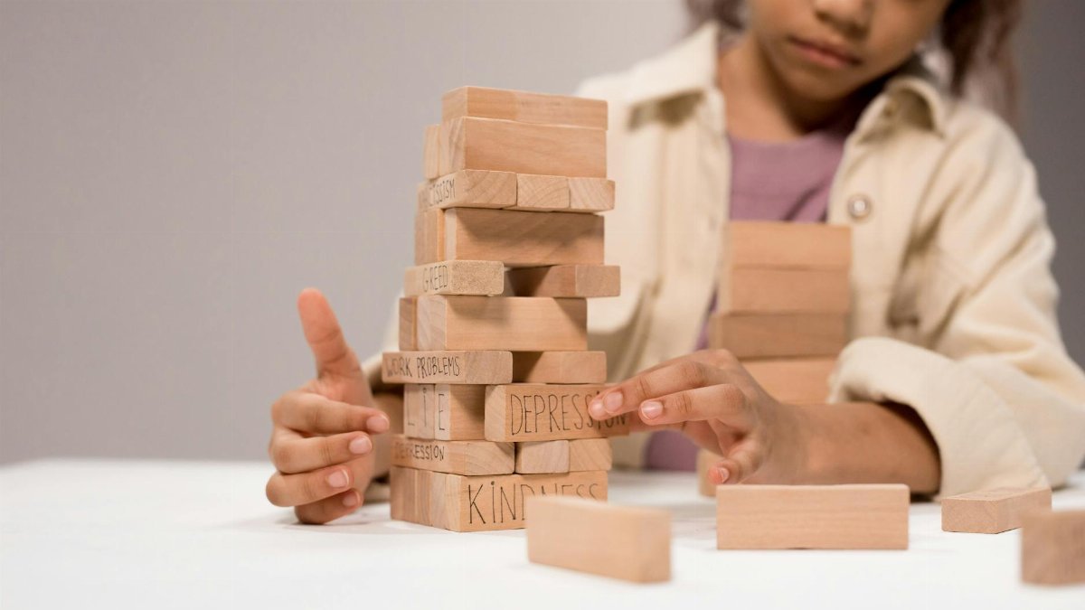 A child thoughtfully stacks wooden blocks with words like 'depression' and 'kindness.'