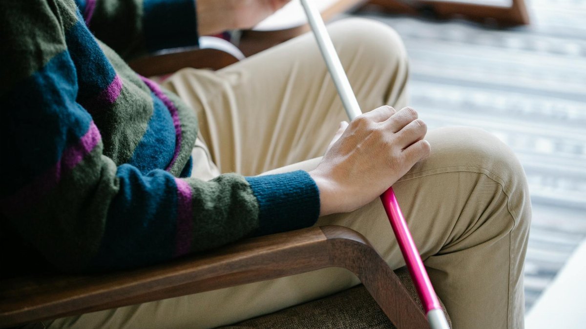 Close-up image of a person holding a walking stick while sitting indoors.