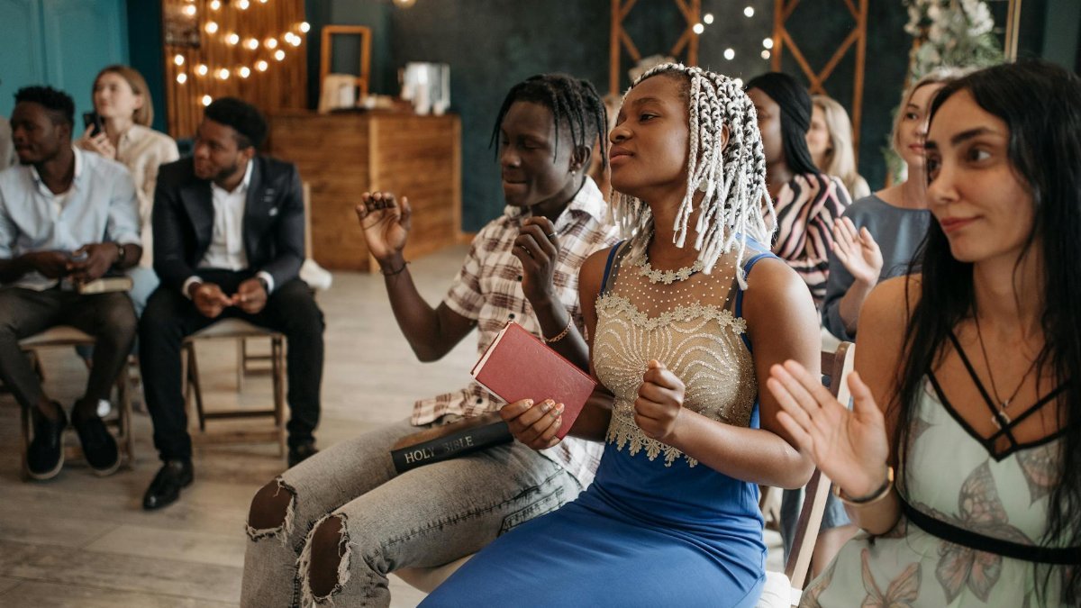 A diverse group of adults engaged in joyful prayer and worship indoors, expressing unity and faith.