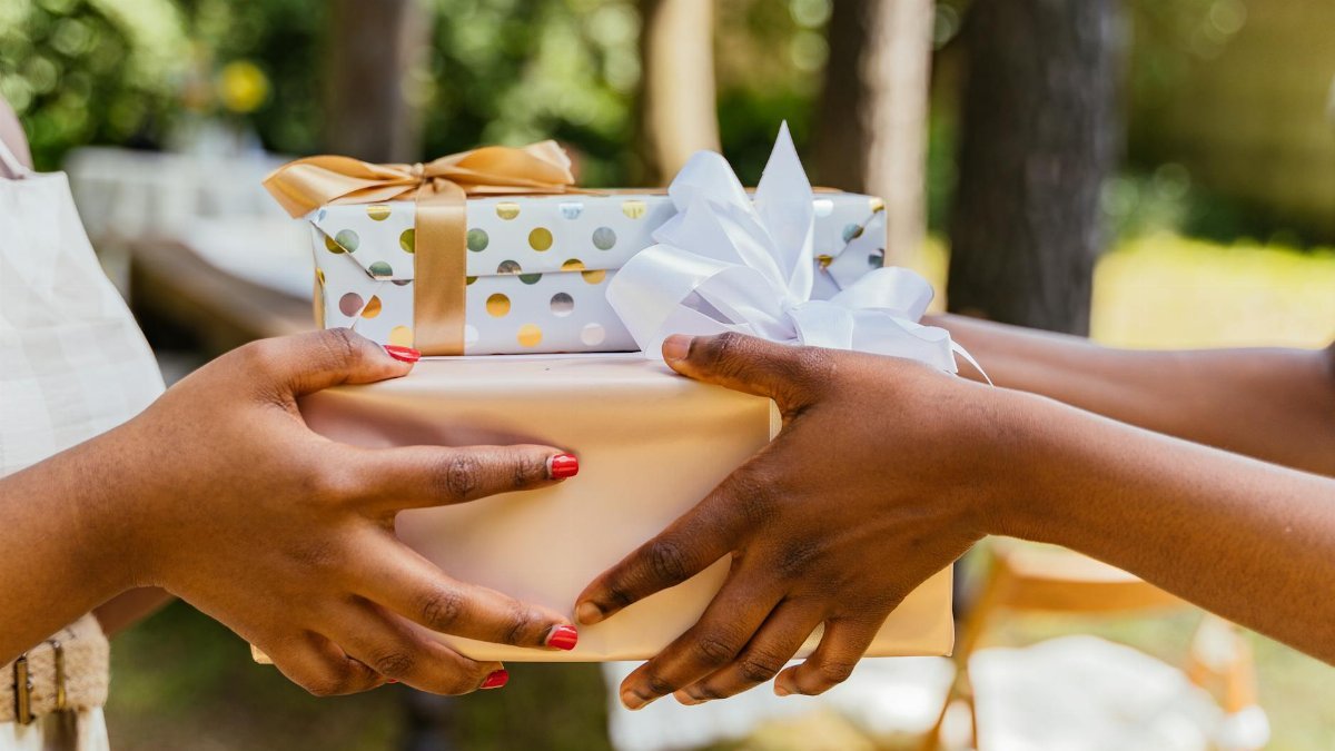 Two people exchange colorful wrapped gifts with bows at an outdoor celebration.