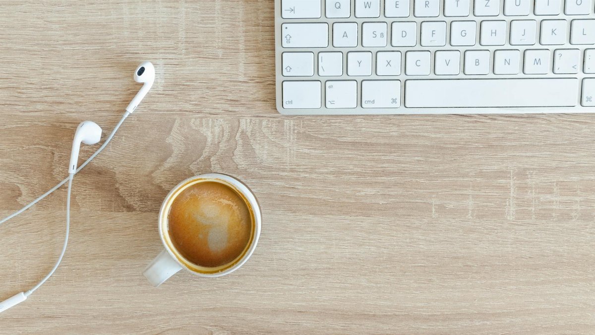 A minimalist desk featuring a keyboard, coffee cup, and earphones on a wooden surface.