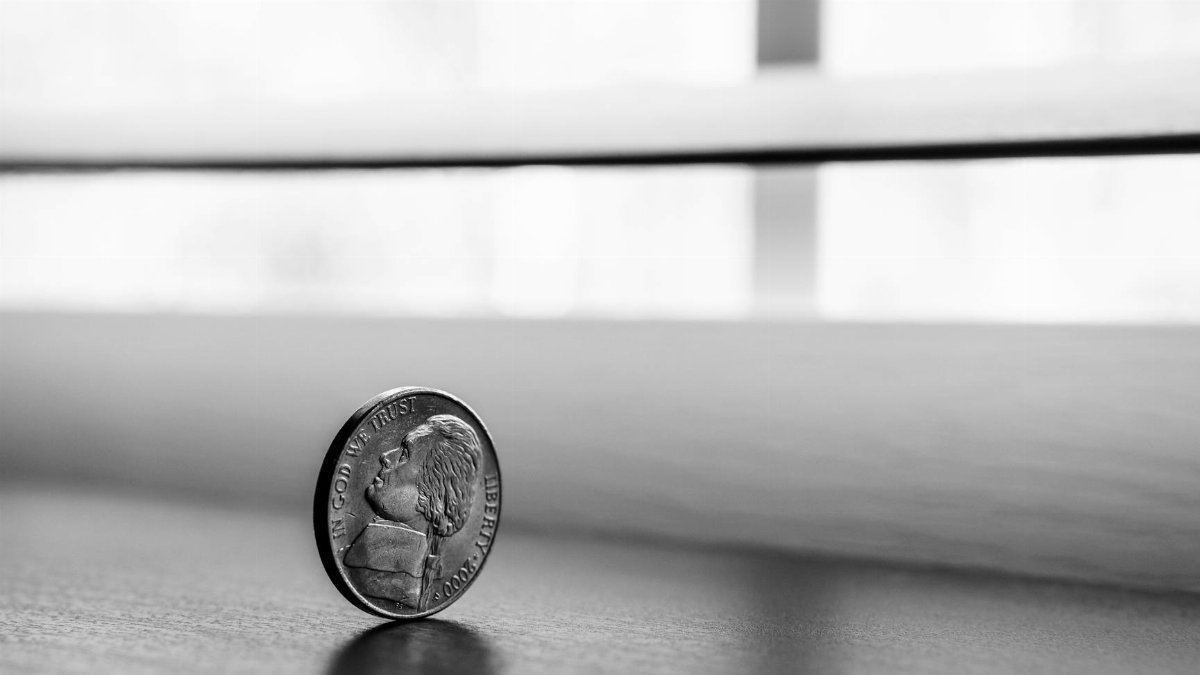 Monochrome close-up of a standing coin reflecting on a smooth surface.