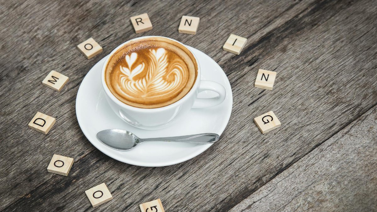 Cup of cappuccino with latte art surrounded by Scrabble letters spelling 'Good Morning'.