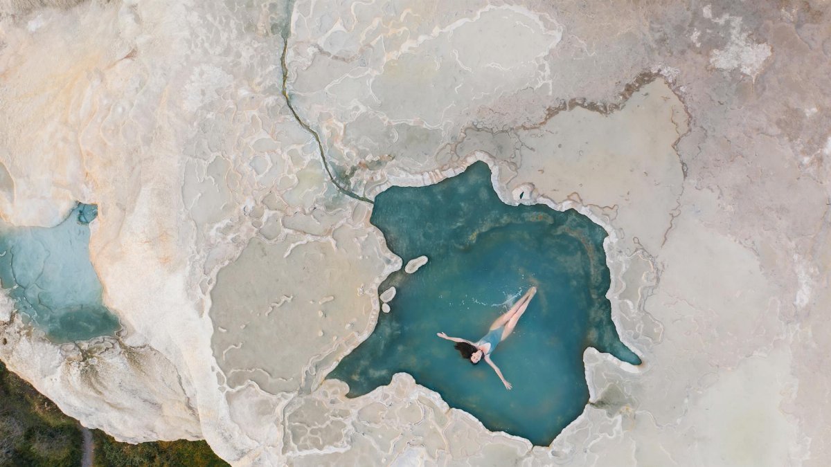 A woman swims in a natural turquoise pool against stunning rock formations in Mexico.
