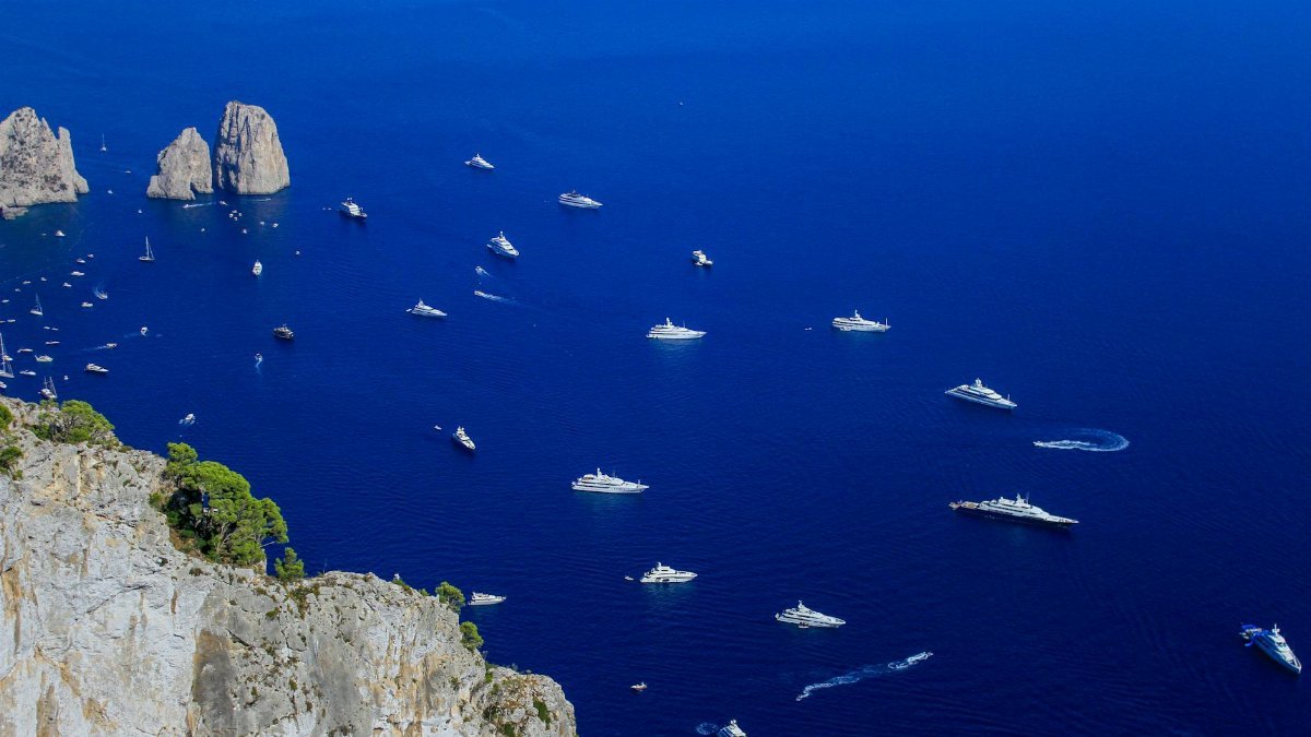 Dramatic aerial shot of yachts off Capri's coast in Campania, Italy, under a clear blue sky.