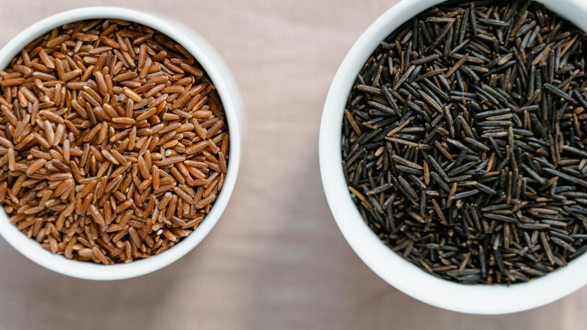 High-angle view of brown and black rice in ceramic bowls on a white surface.