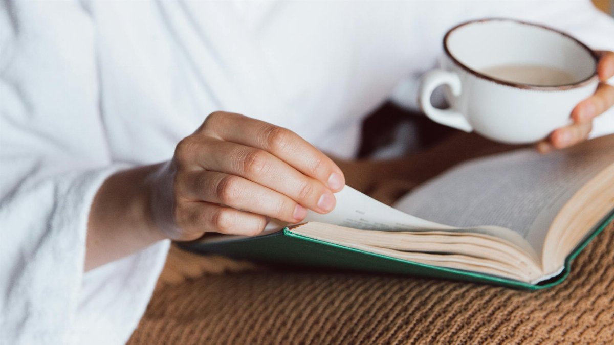 A person enjoys a peaceful morning with a book and a cup of coffee, wrapped in a cozy robe.