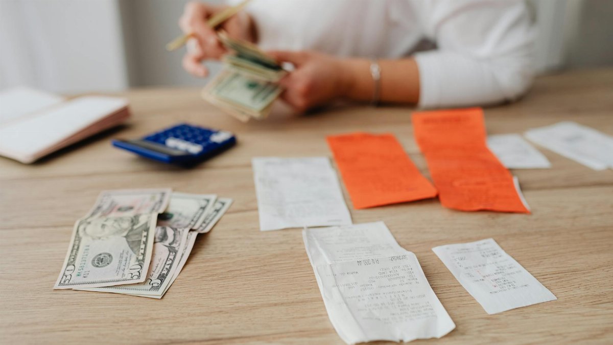 A person using a calculator and cash to plan a household budget.