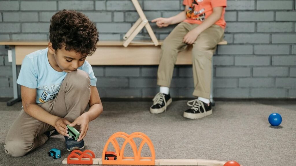 Two kids enjoying creative play with wooden toy tracks in a classroom setting.