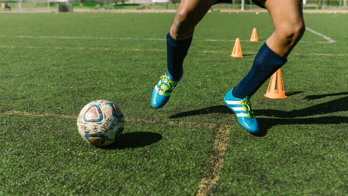 Dynamic image of a soccer player practicing drills on a grass field with vibrant shoes and cones.