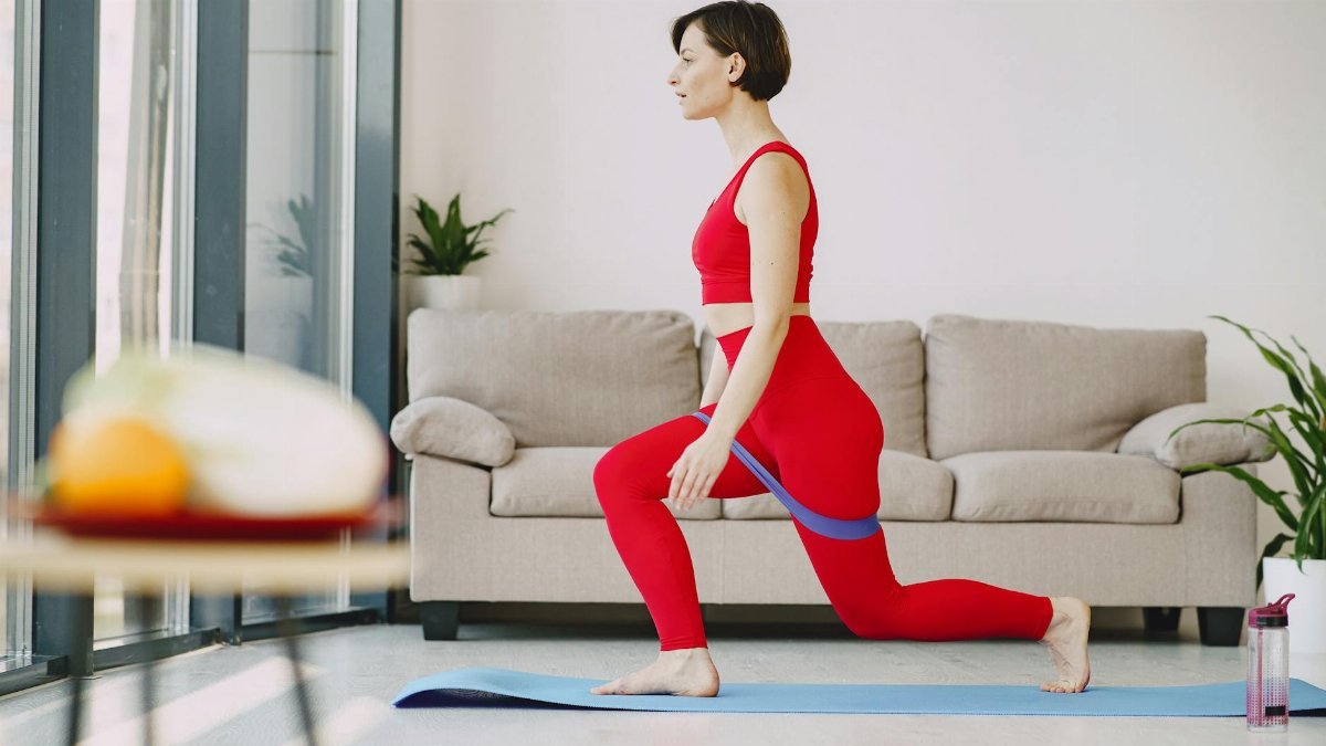 Woman in red outfit performing yoga lunge exercise indoors with resistance band.