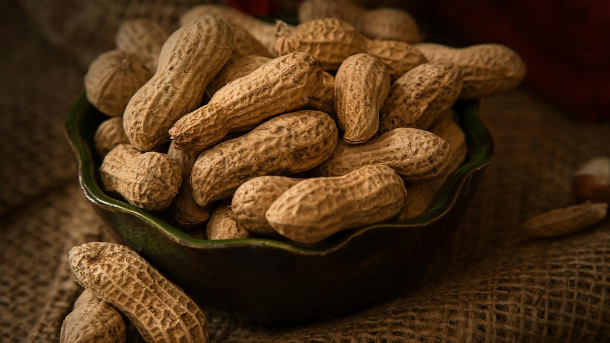 A rustic bowl filled with whole peanuts resting on a burlap cloth, evoking a natural and earthy feel.